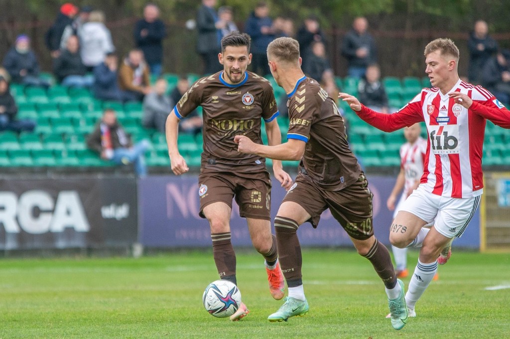 Three football players, two in dull colours, a third in red and white stripes