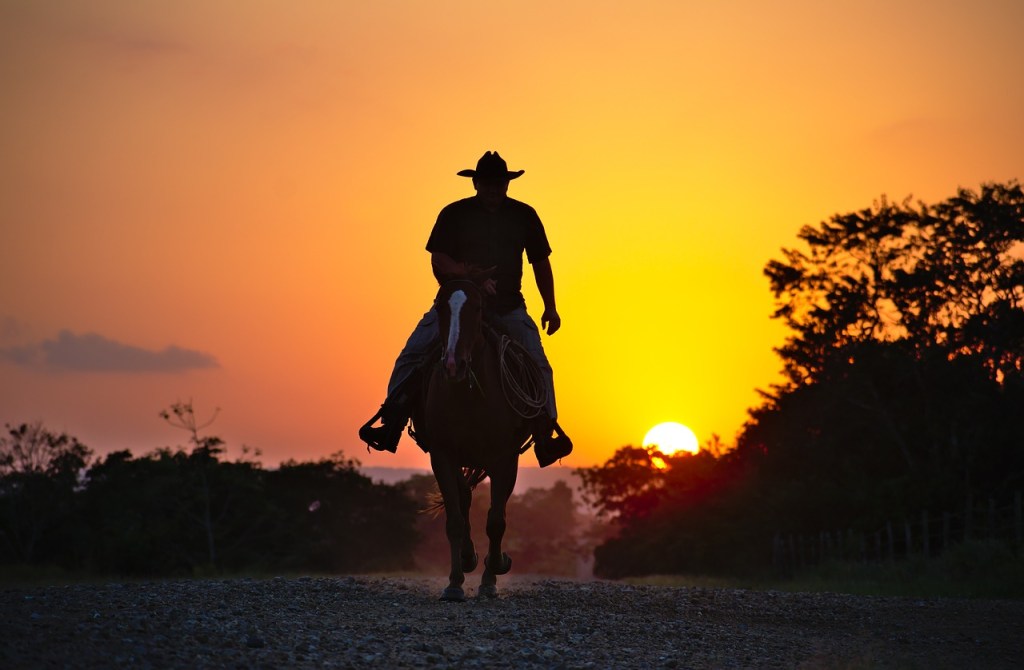 Pony express - cowboy galloping on horse at sunset