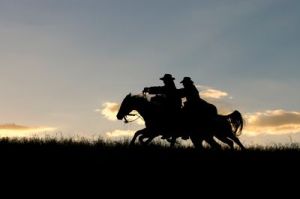2 cowboys riding hard on the horizon