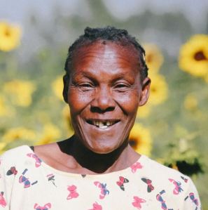 An african woman smiling in front of a field of sunflowers.