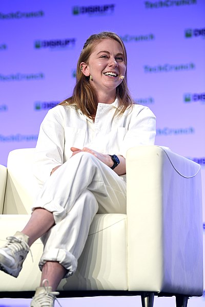 Simone Giertz sat on a white chair on the stage laughing while speaking at Techcrunch Disrupt