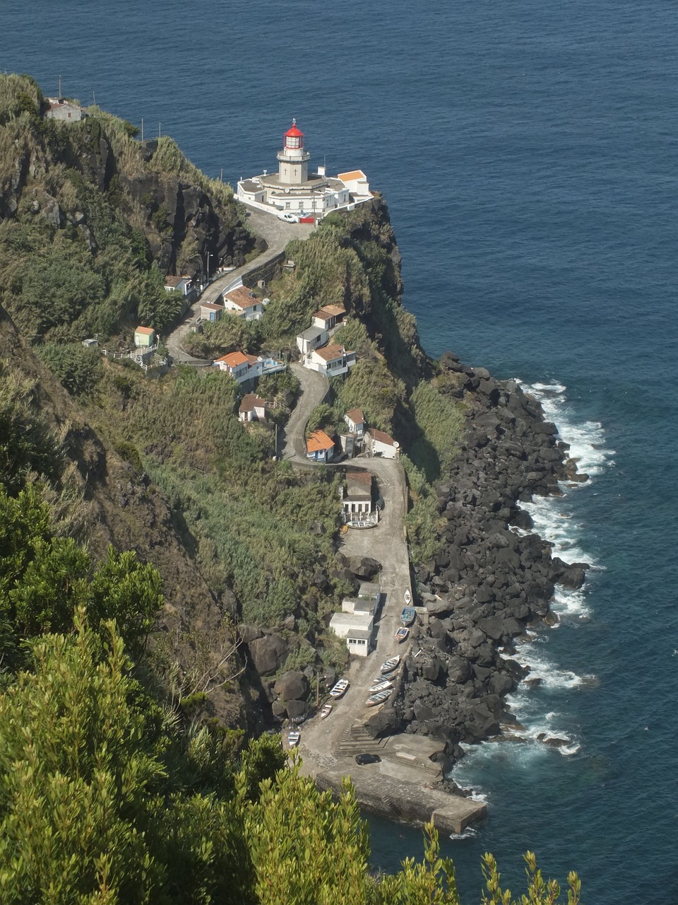An aerial photograph of São Miguel lighthouse in the Azores showing the surrounding tree-covered cliff and winding road.