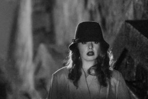 A black and white image of a women on outside stairs wearing har and raincoat.