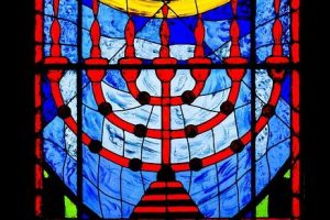 A colourful stainglass window showing a menorah (seven branched curving candlestick)