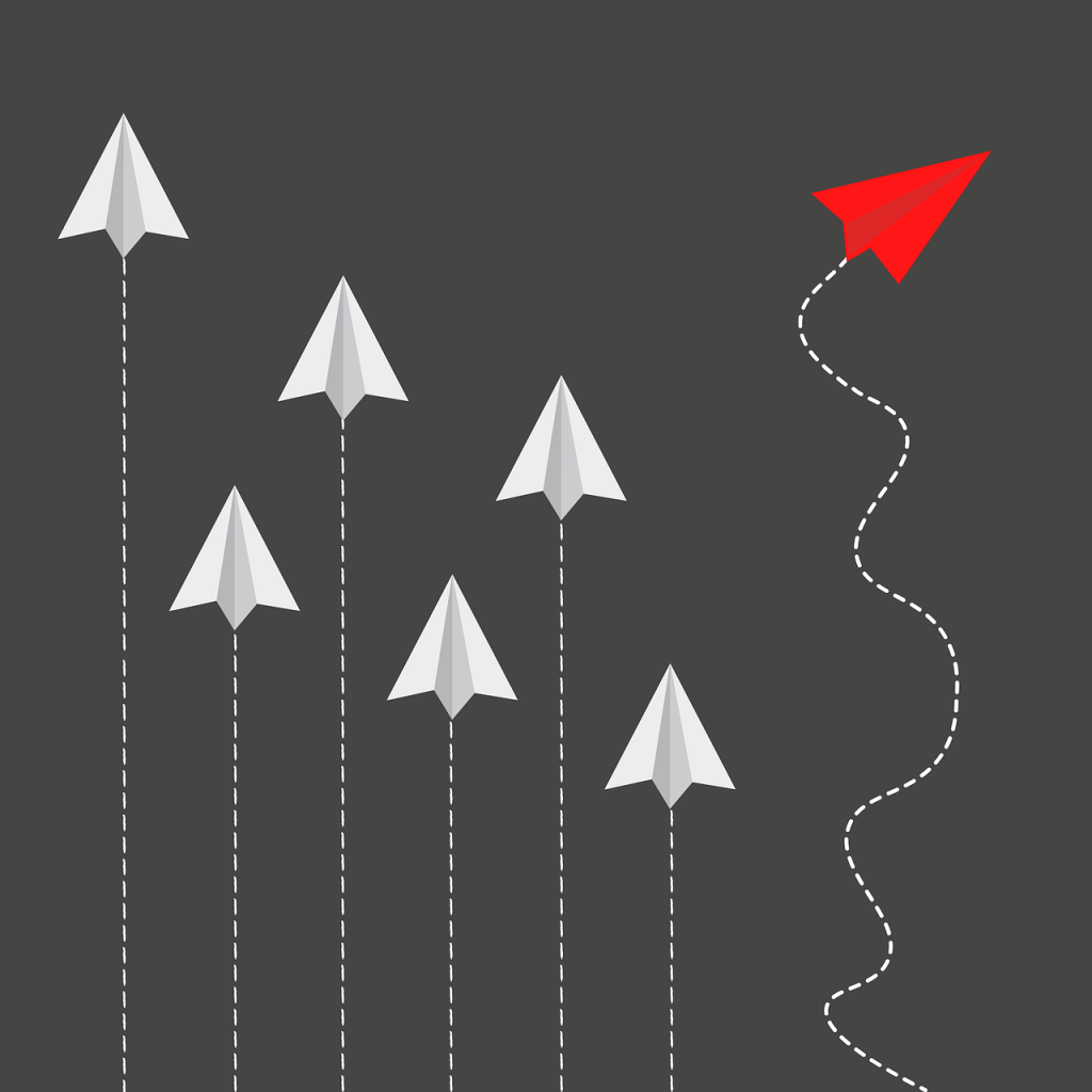 5 paper planes going in the same straight line with one red one on a different curved path
