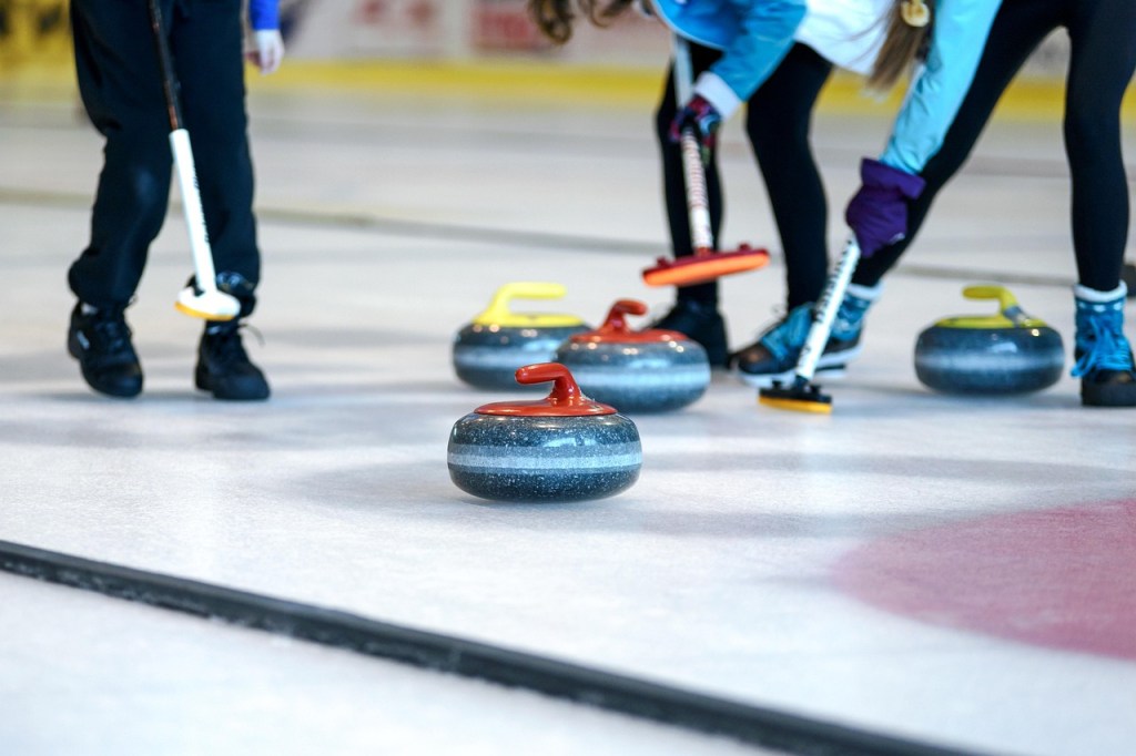 Curlers sweeping in front of a stone amongst other stones.